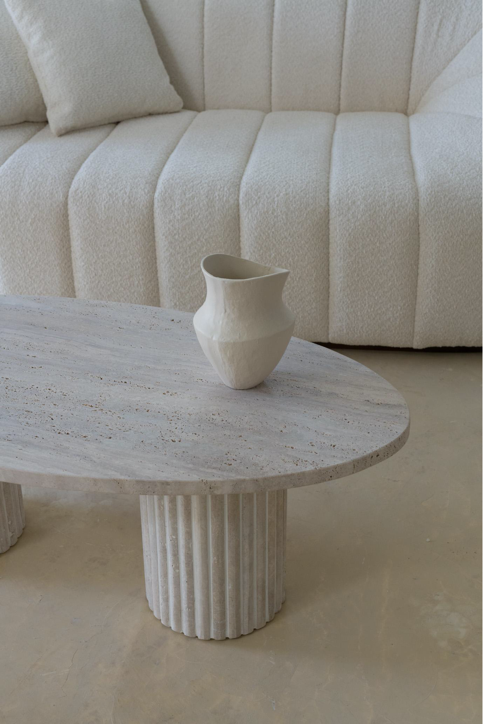 Gros plan sur une table basse ovale en travertin, finition naturelle et texture brute.