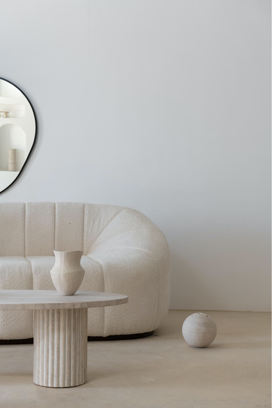 Ambiance chaleureuse avec une table basse ovale en travertin, harmonie de matières naturelles.