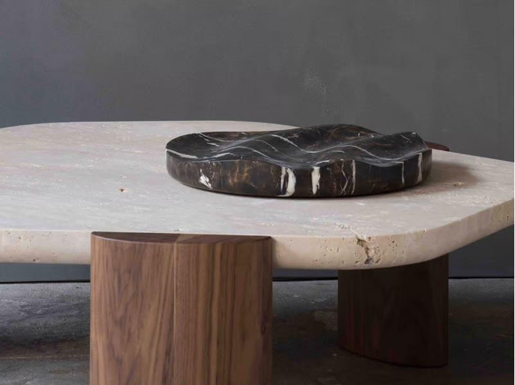 Vue rapprochée d’une table basse en travertin avec un plateau irrégulier et des pieds en bois massif.